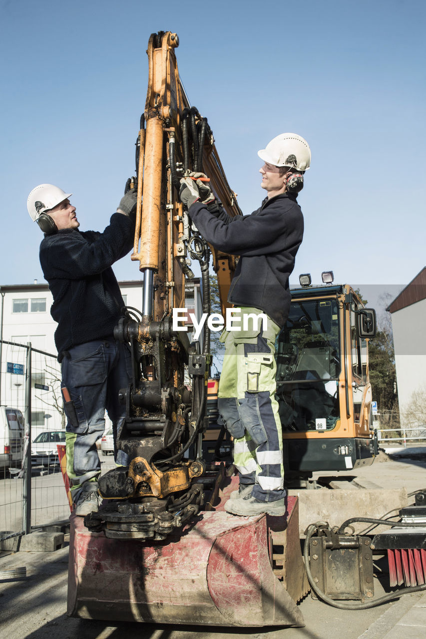 Side view of construction workers using excavator against blue sky