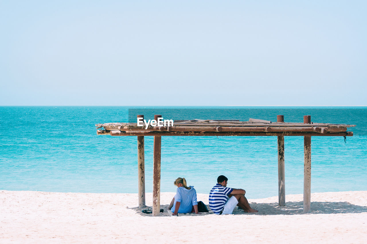 Friends sitting on beach against clear sky