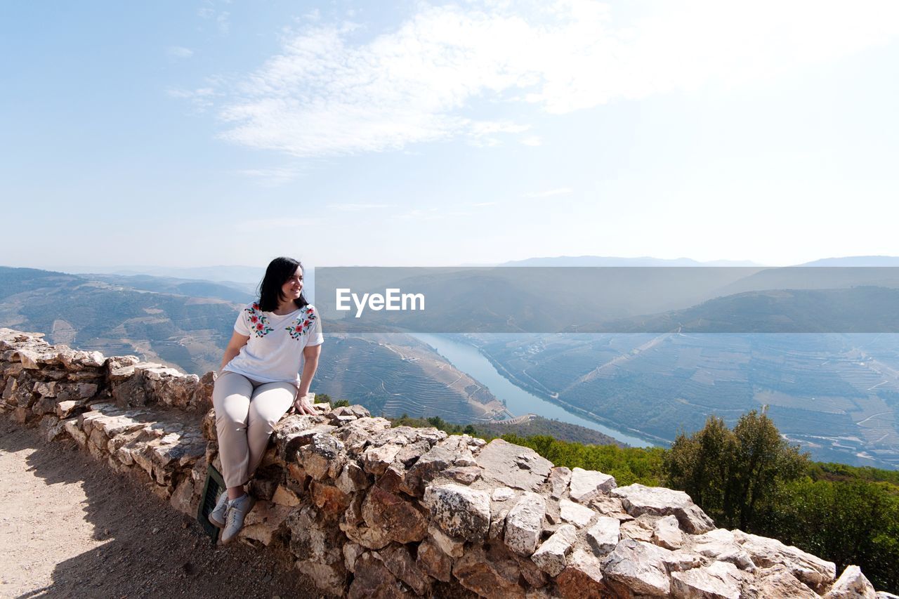 Woman sitting on retaining wall against mountains