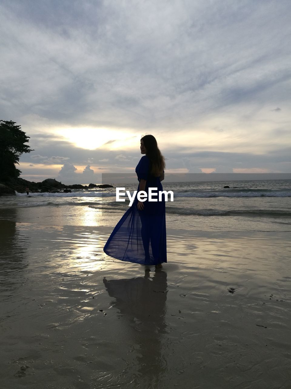 Woman standing on shore at beach against sky during sunset