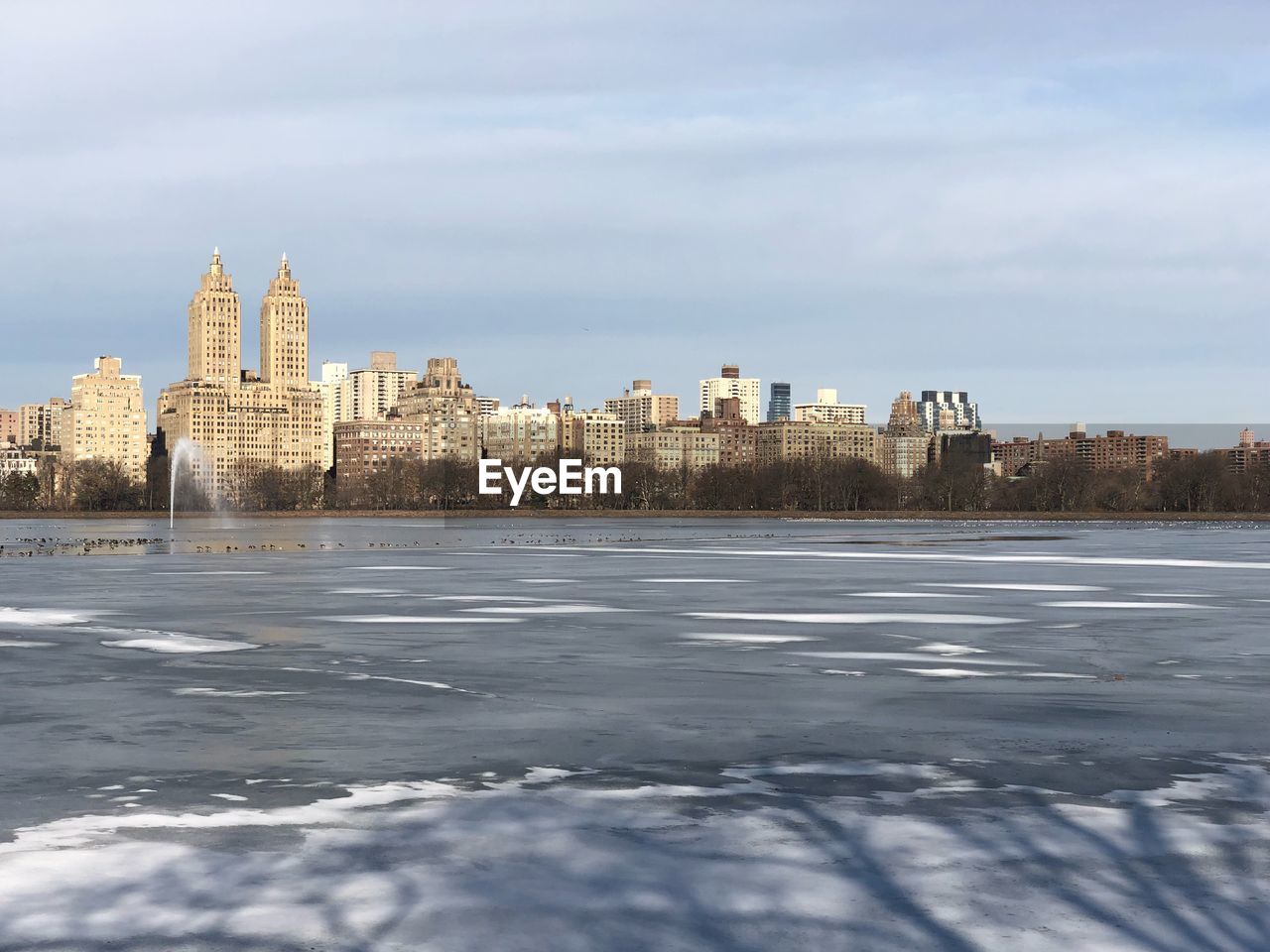View of frozen river by buildings against sky