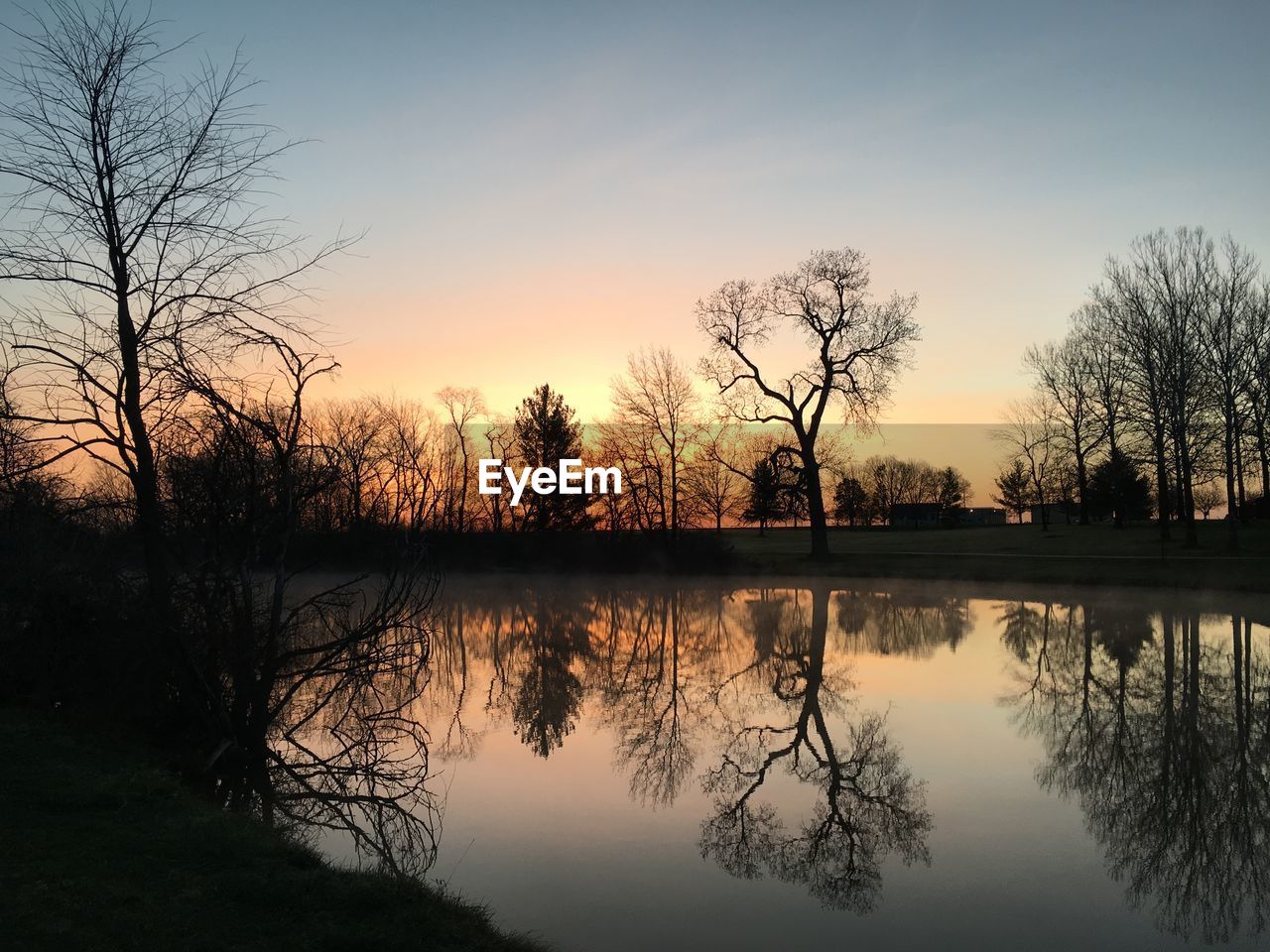 Silhouette trees by lake against sky during sunset