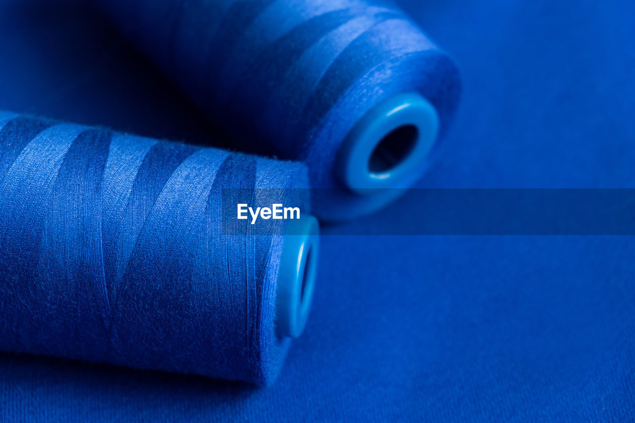 Texture of blue thread in spool for sewing on a plain blue background. clothing sewing material