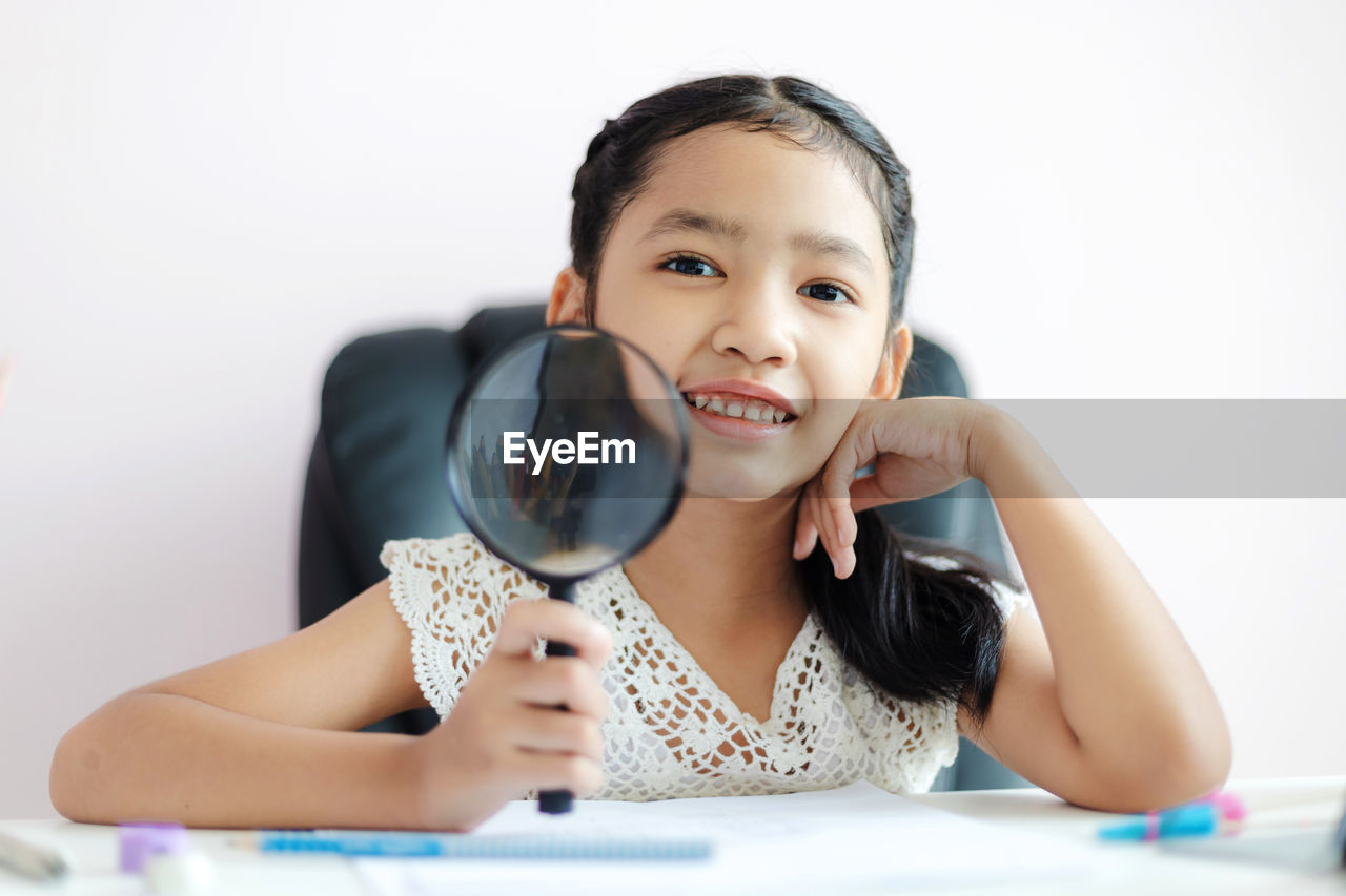 Portrait of cute girl holding magnifying glass against white background