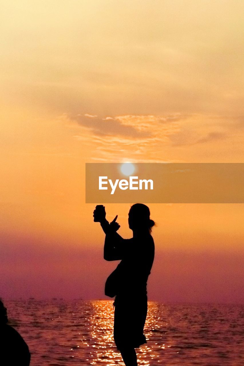 Silhouette man standing by sea against sky during sunset