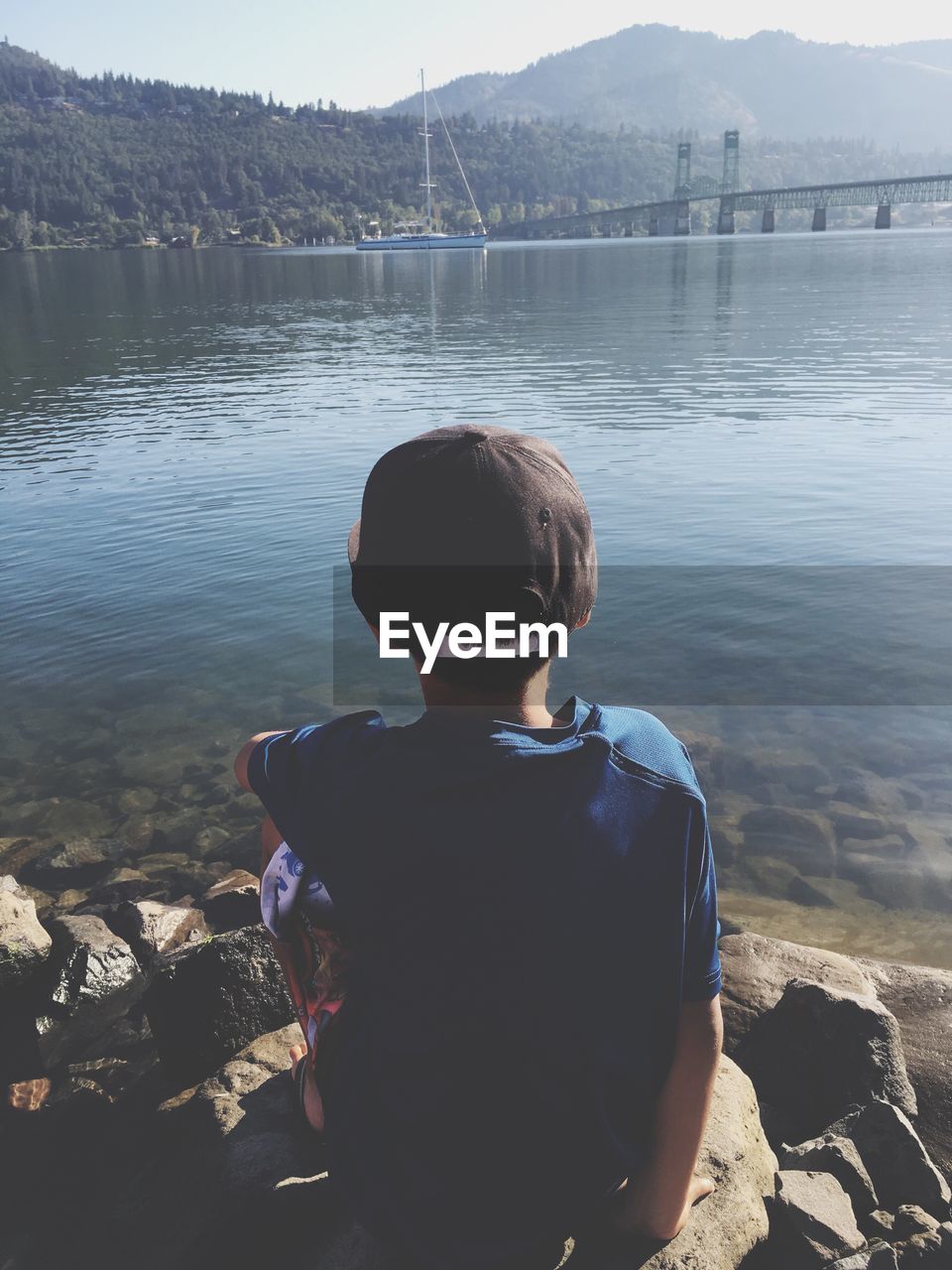 Rear view of boy sitting on rocks at lakeshore