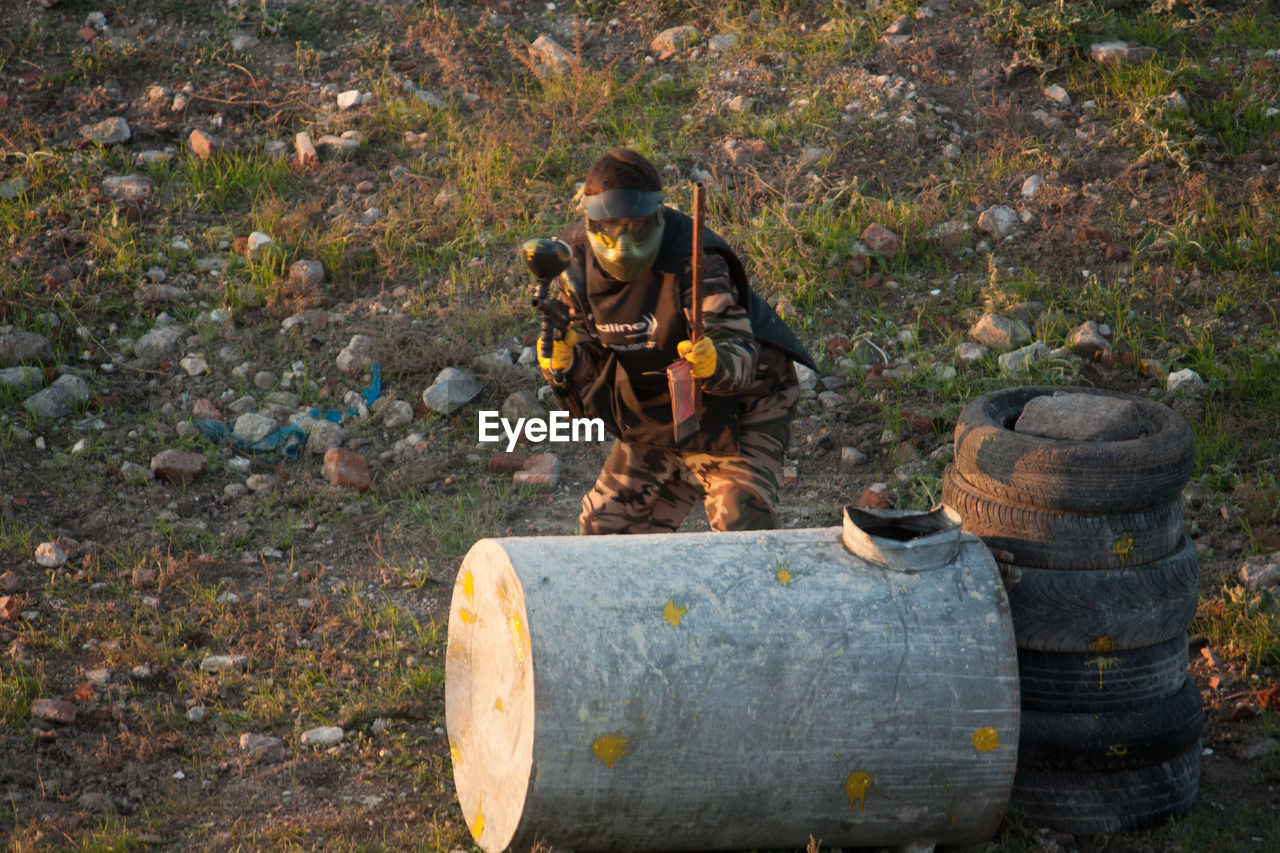 Army soldier hiding behind drum and tire