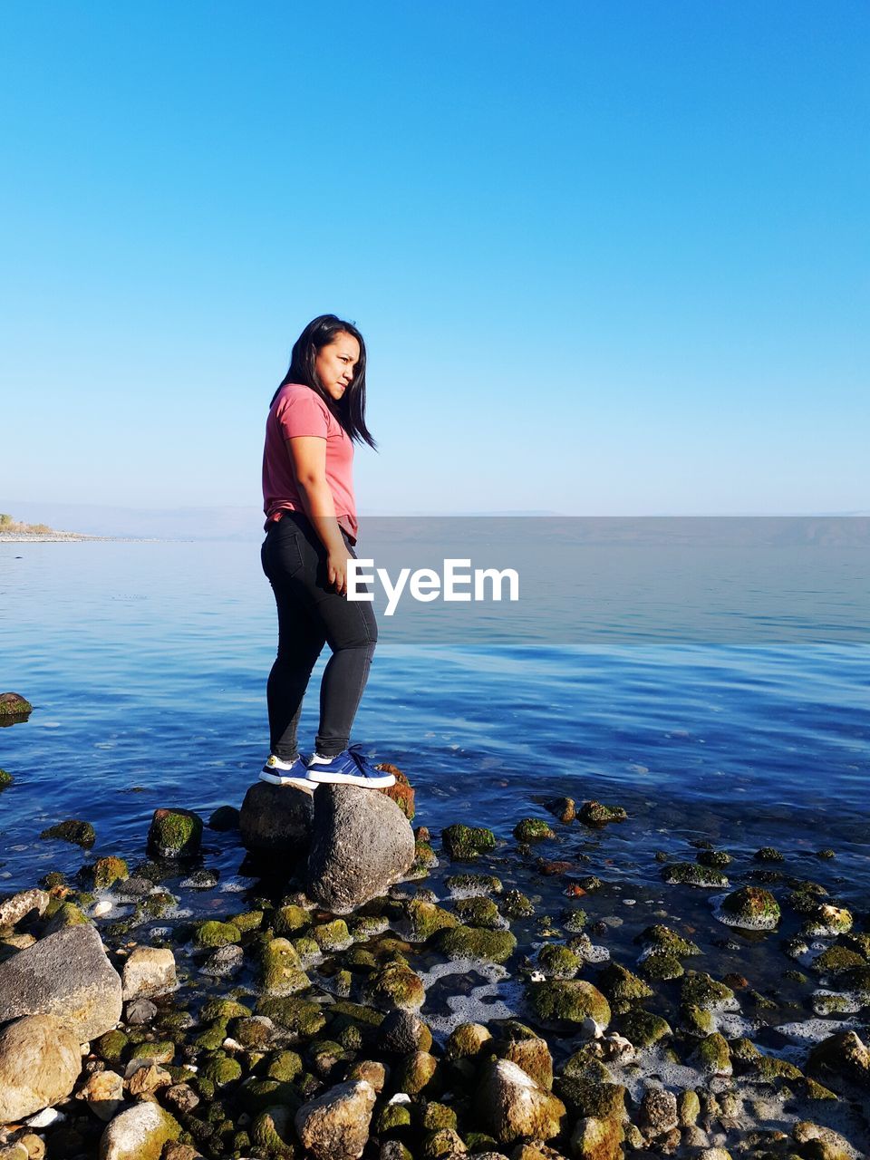 Young woman standing on rock by sea against clear sky