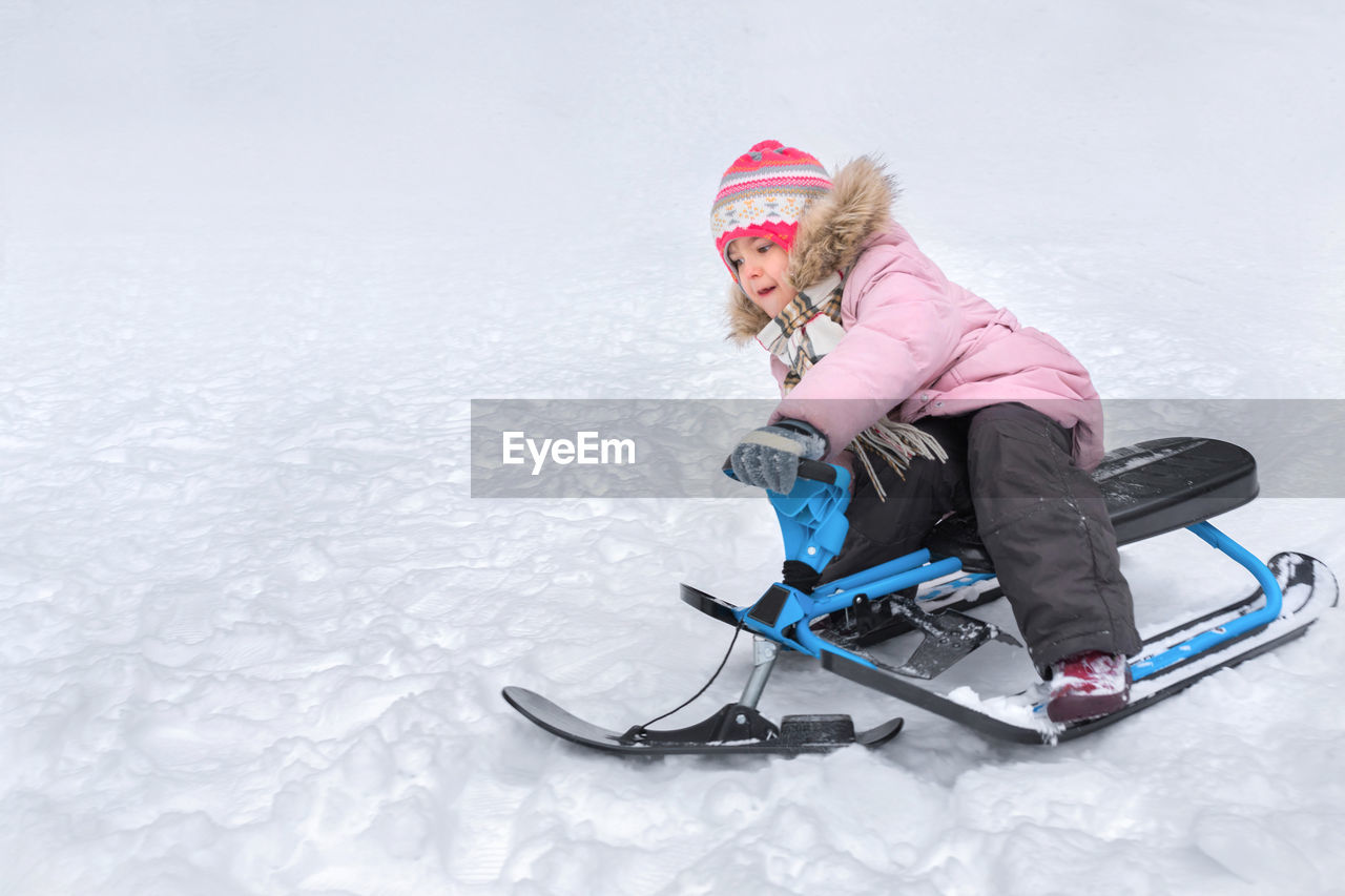 winter, snow, cold temperature, winter sports, child, sled, one person, childhood, fun, full length, clothing, women, leisure activity, warm clothing, sports, holiday, emotion, female, happiness, nature, hat, mountain, smiling, vacation, enjoyment, lifestyles, footwear, blond hair, trip, skiing, snowboarding, knit hat, glove, adult, tobogganing, sports equipment, ice, sledding, ski-wear, ski holiday, recreation, frozen, sitting, positive emotion, motion, copy space, day, activity, teenager, white, outdoors