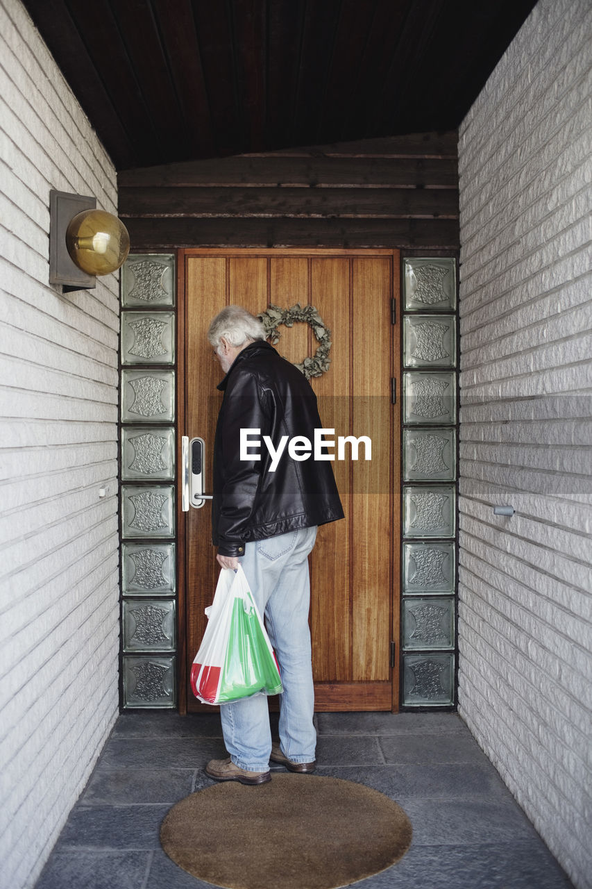 Rear view of man carrying bag opening door