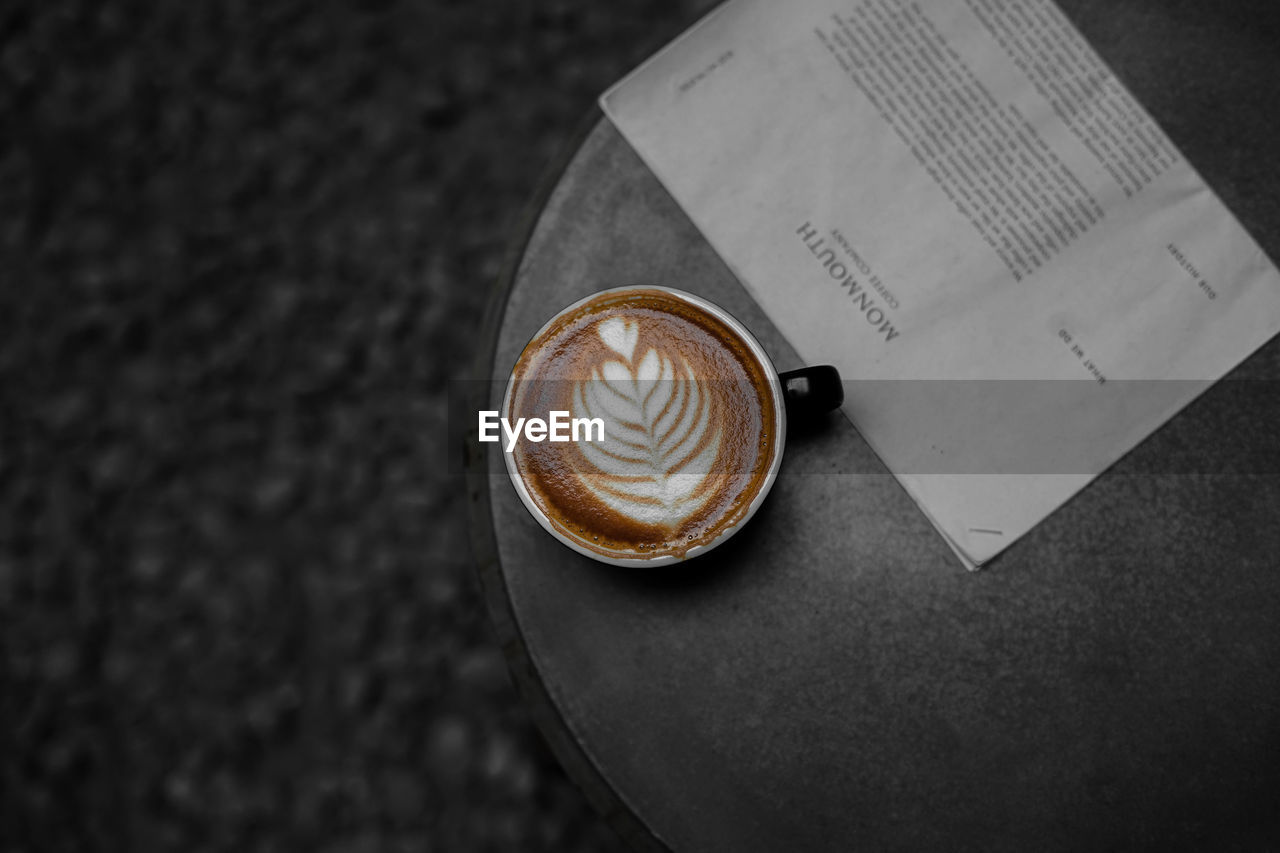 High angle view of coffee in cup by newspaper on table