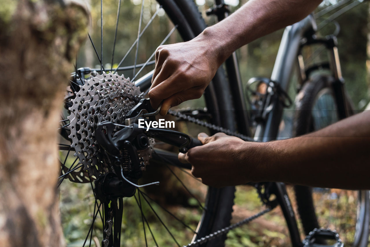 Cropped male cyclist fixing mechanism of bicycle against hiker setting in forest