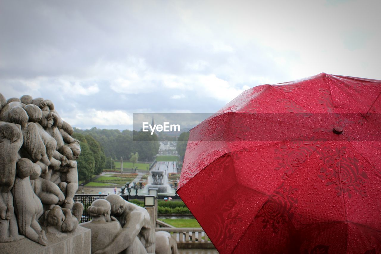 Red umbrella by statues against cloudy sky during monsoon