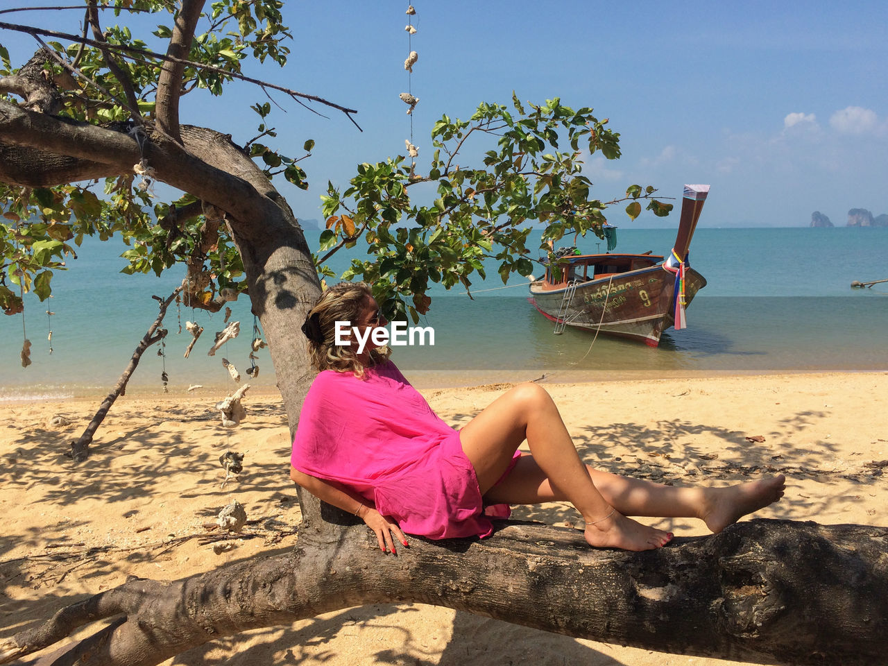Full length of woman relaxing on tree trunk at beach against sky