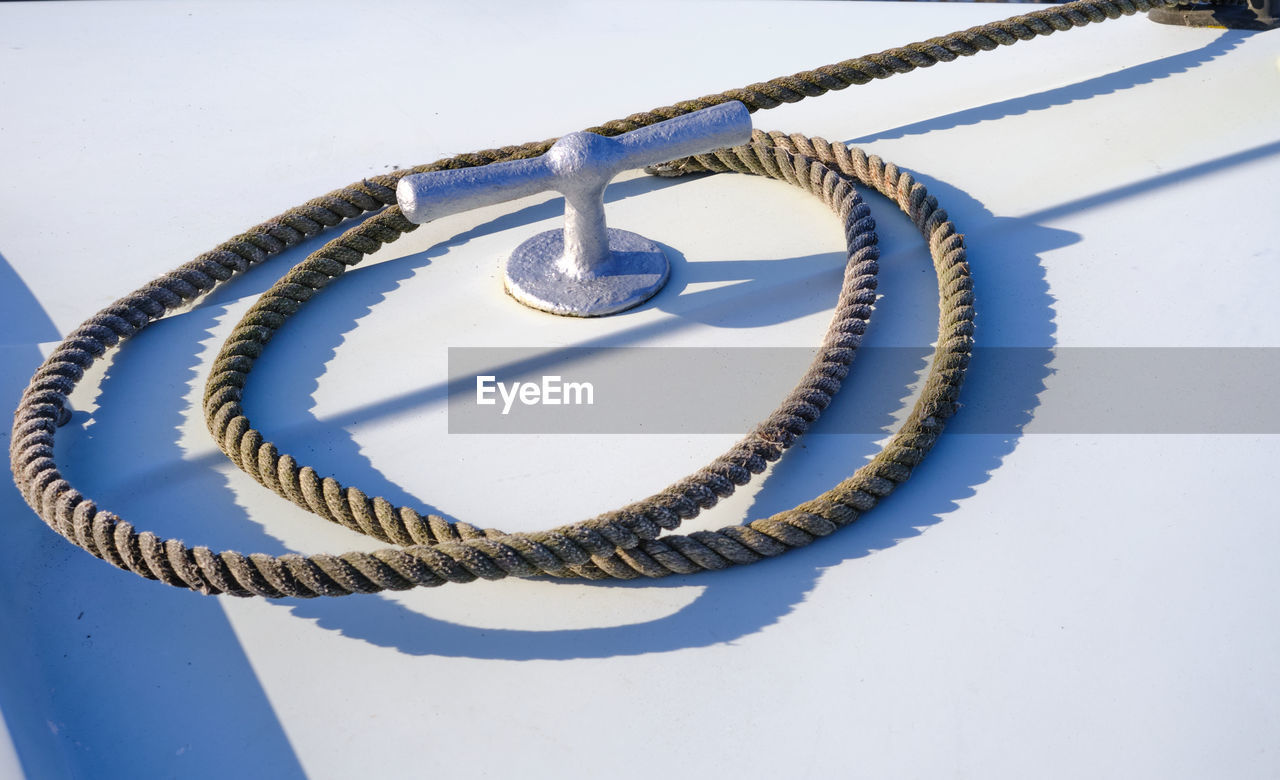 Close-up of nautical mooring rope circling around a cleat against a white background