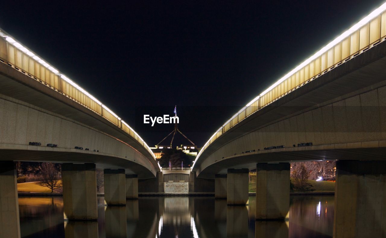 Illuminated bridge over river against sky at night