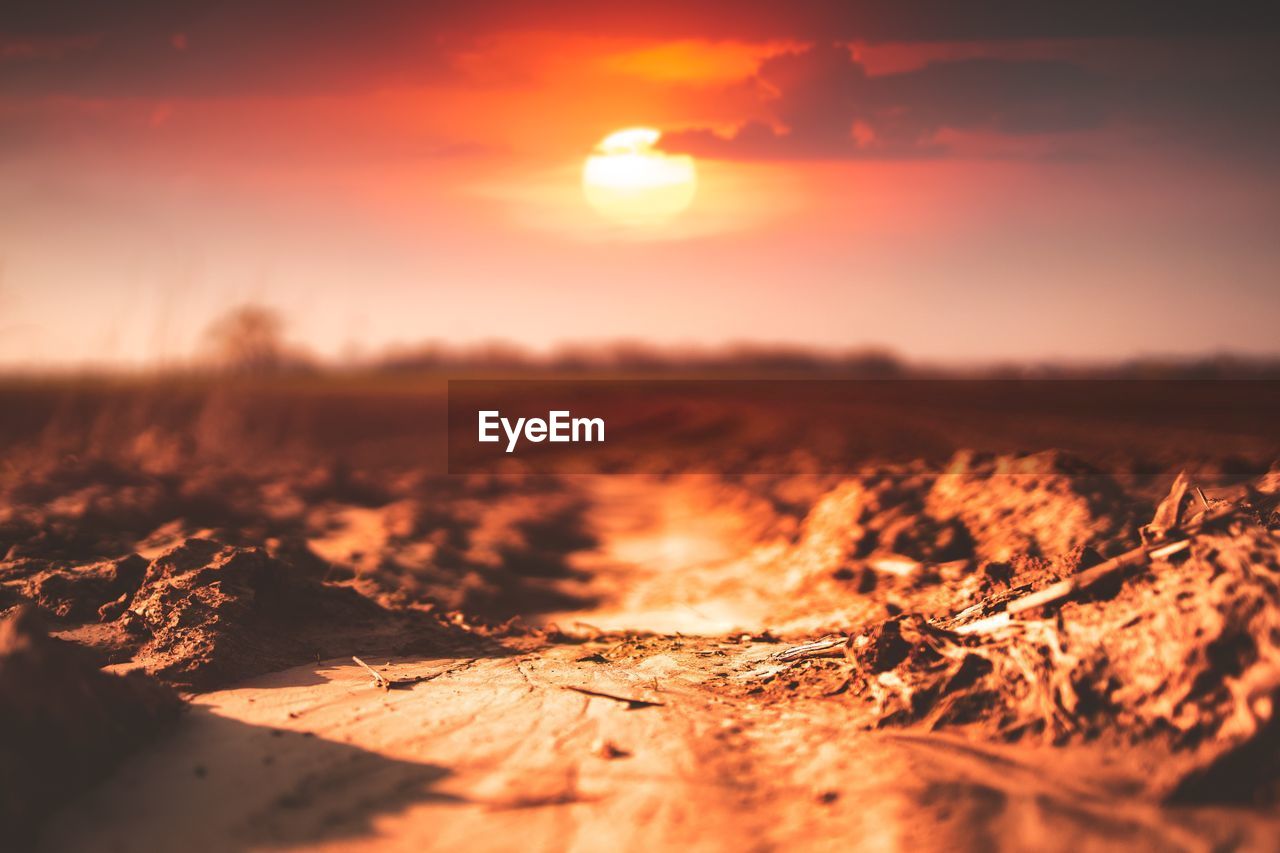 SURFACE LEVEL OF DIRT ROAD AGAINST SKY DURING SUNSET