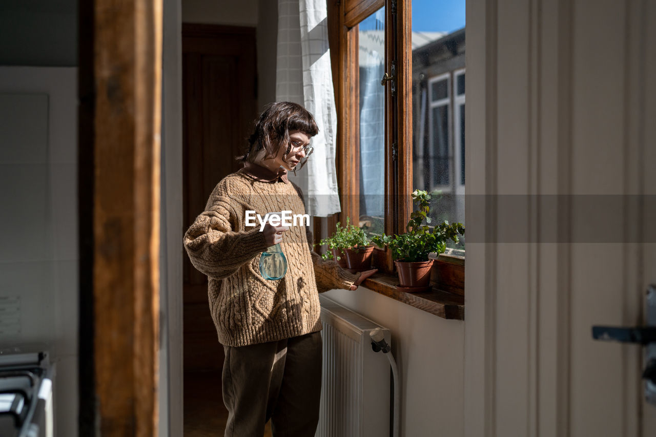 Teenager plant lover moistening green leaves of plants. domestic life of girl living in old house