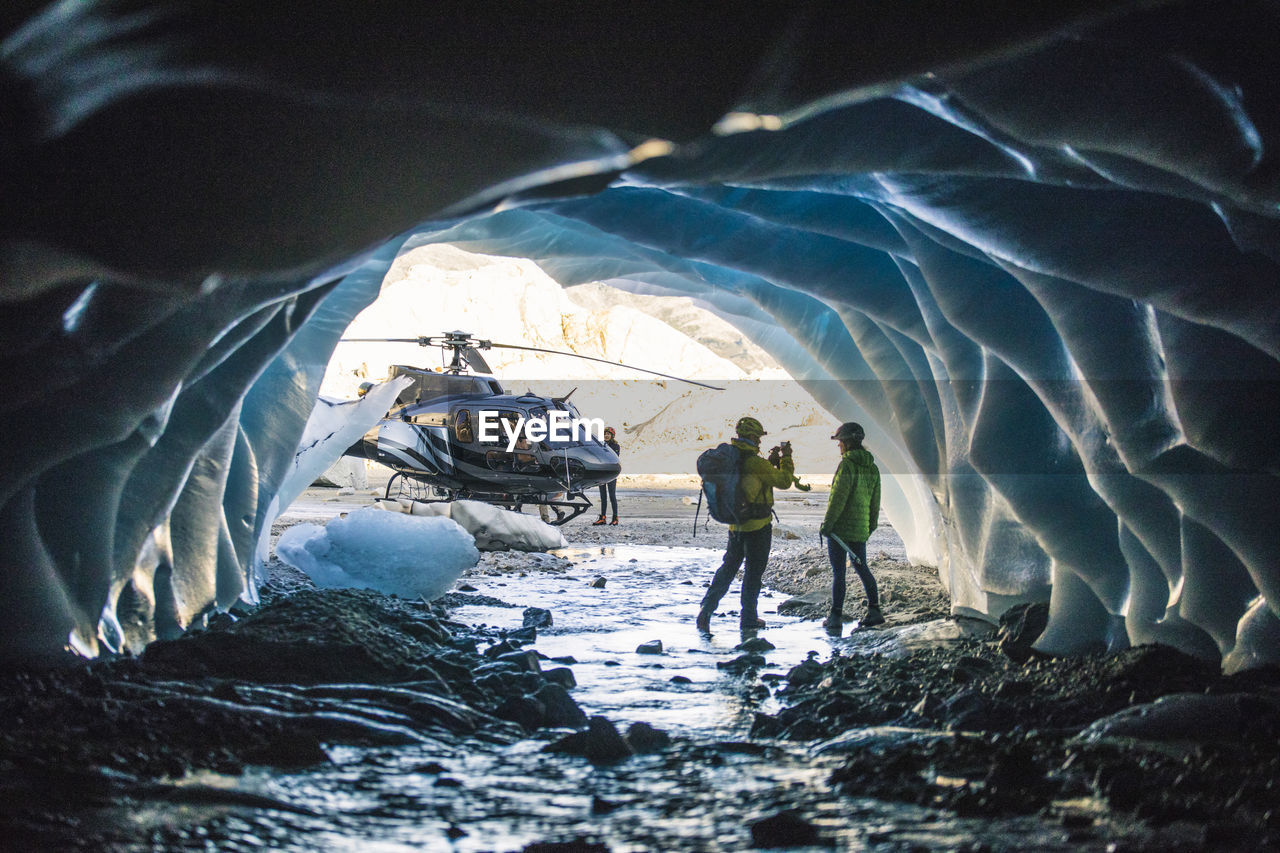 Man photographing partner in ice cave during helicopter tour.