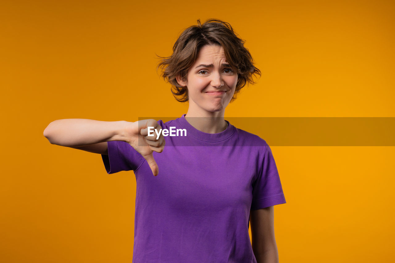 portrait of young woman standing against orange background