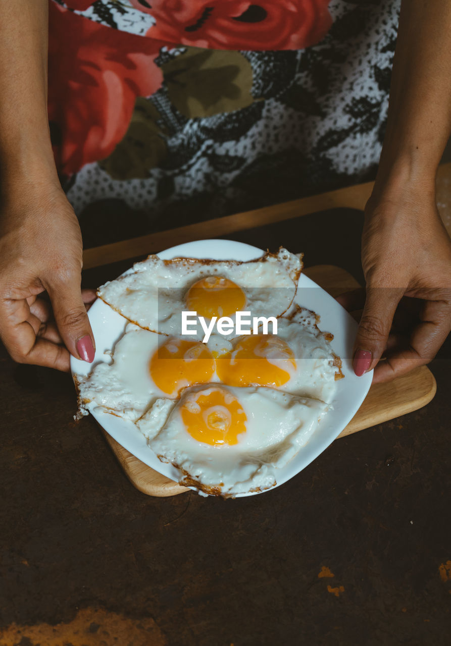 Midsection of woman holding fried eggs in plate on table