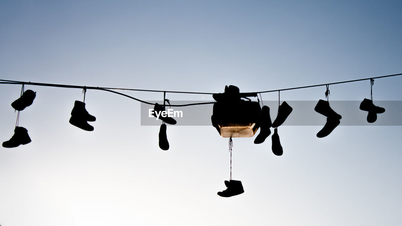 Low angle view of silhouette shoes hanging on cable against clear sky at sunset