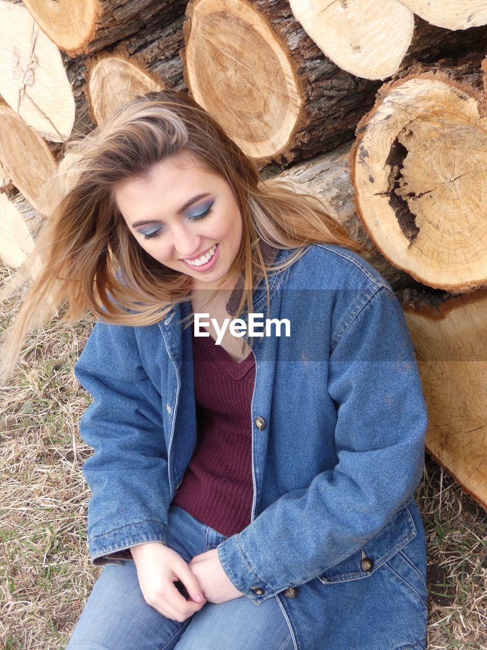 Cheerful young woman wearing denim jacket sitting by logs