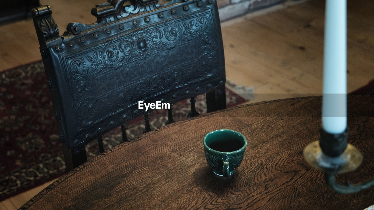 Close up view of artisanal tea cup on wooden table with old vintage wood royal armchair 