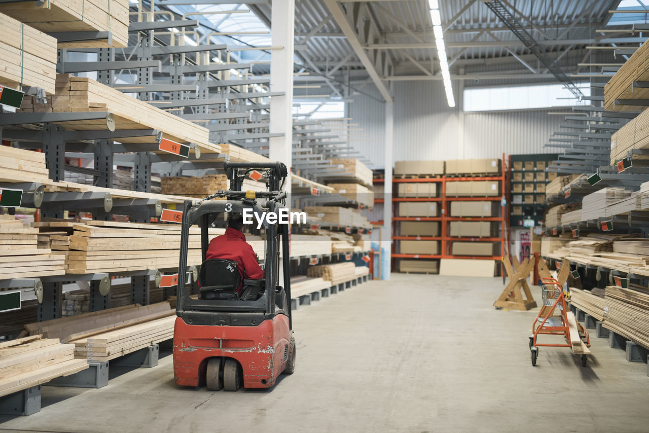 Rear view of salesman driving forklift in warehouse at hardware store