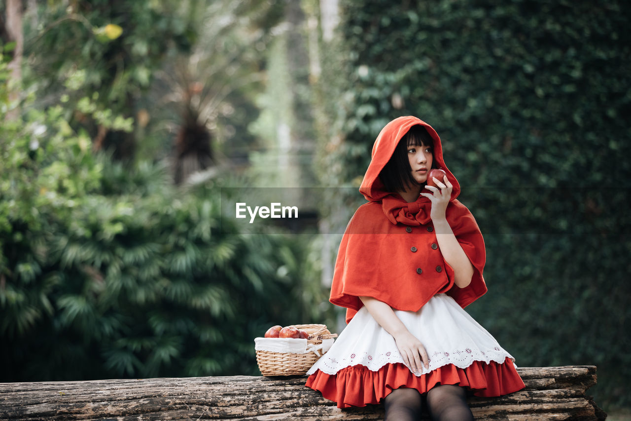 Woman with red umbrella sitting against trees