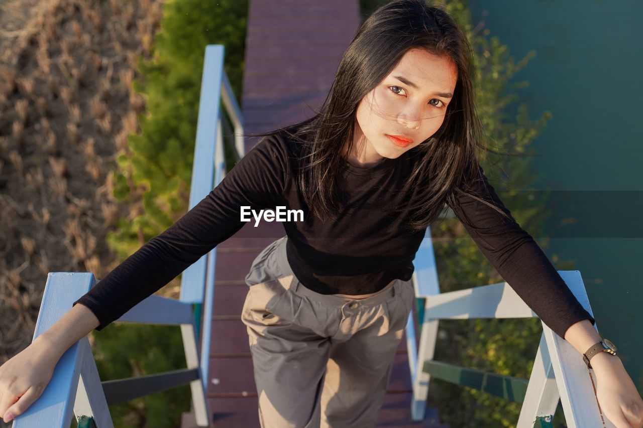 Portrait of beautiful young woman standing against railing