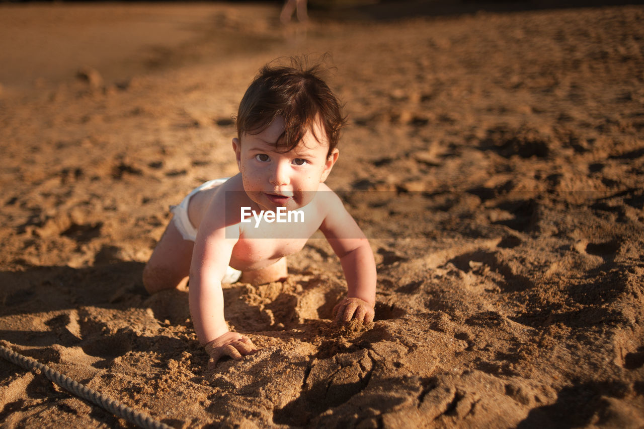 PORTRAIT OF SHIRTLESS BOY LYING ON SAND IN MUD