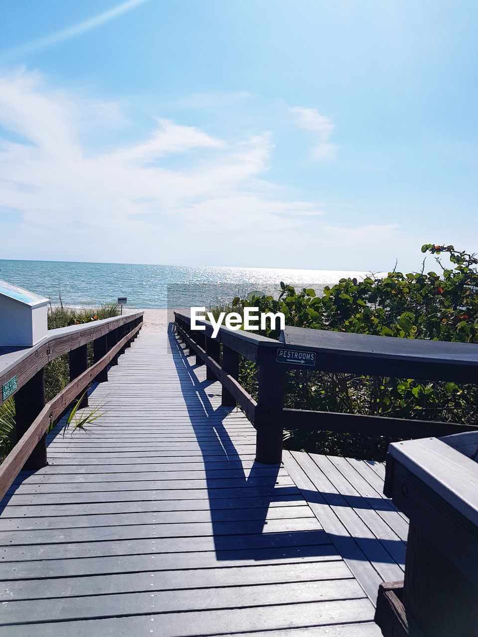 Empty wooden walkway by sea against sky