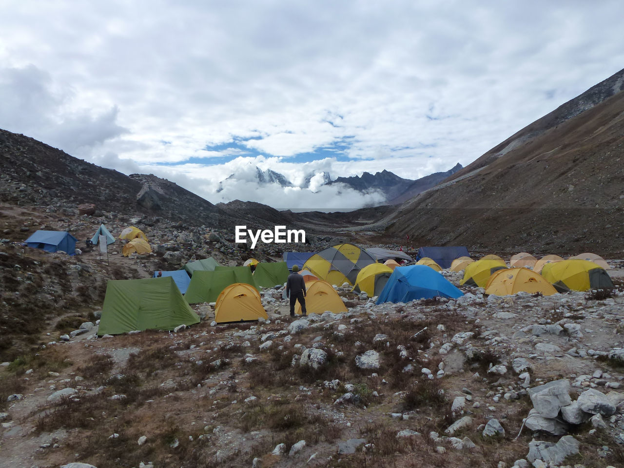 Rear view of man standing by tents at mountains against cloudy sky