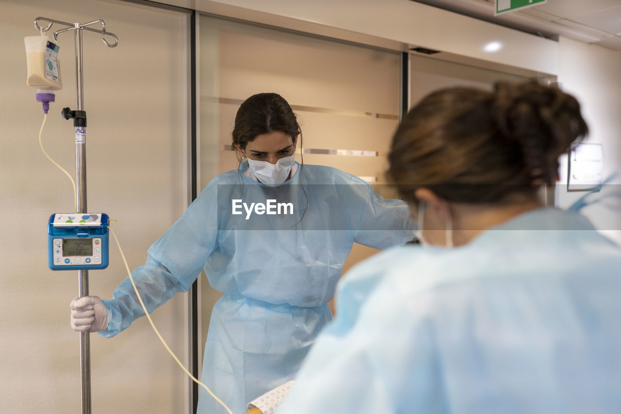 Two nurses help a patient walk in a hallway