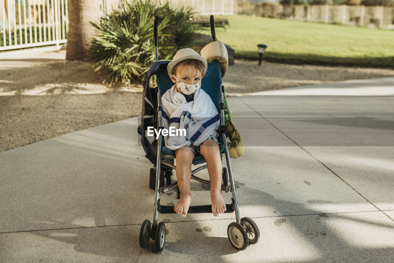 Portrait of young boy with mask on in stroller outside on vacation
