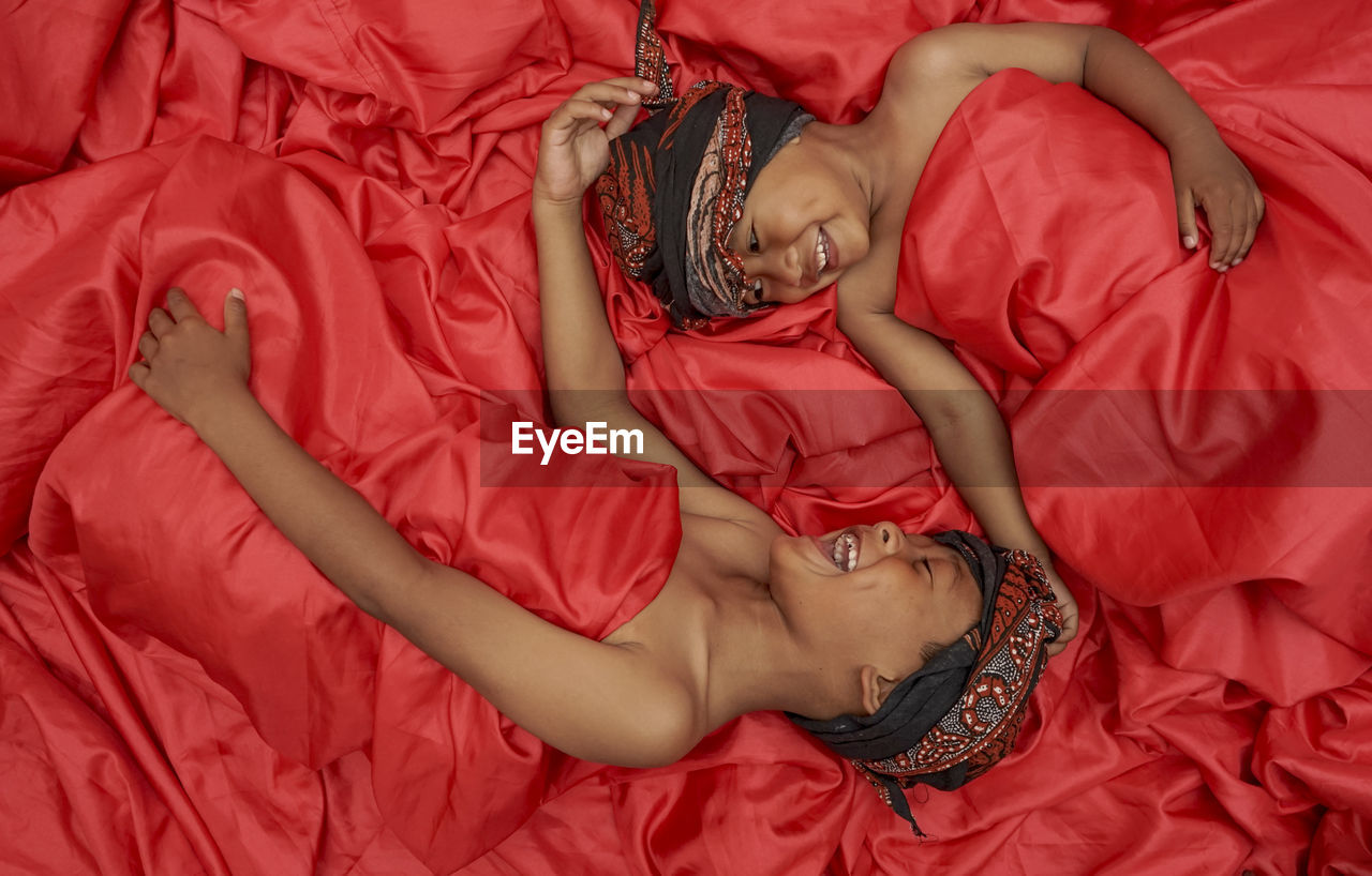 High angle view of boys lying down on red textile