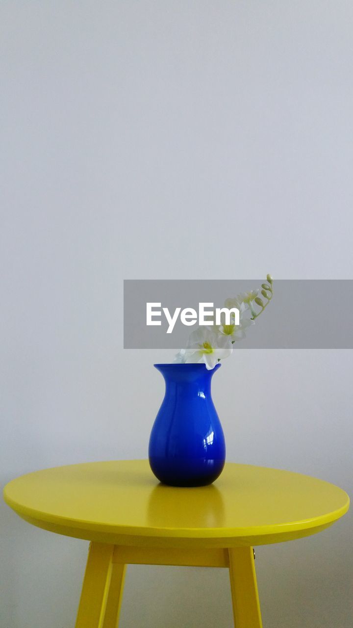 Flower vase on yellow table against wall