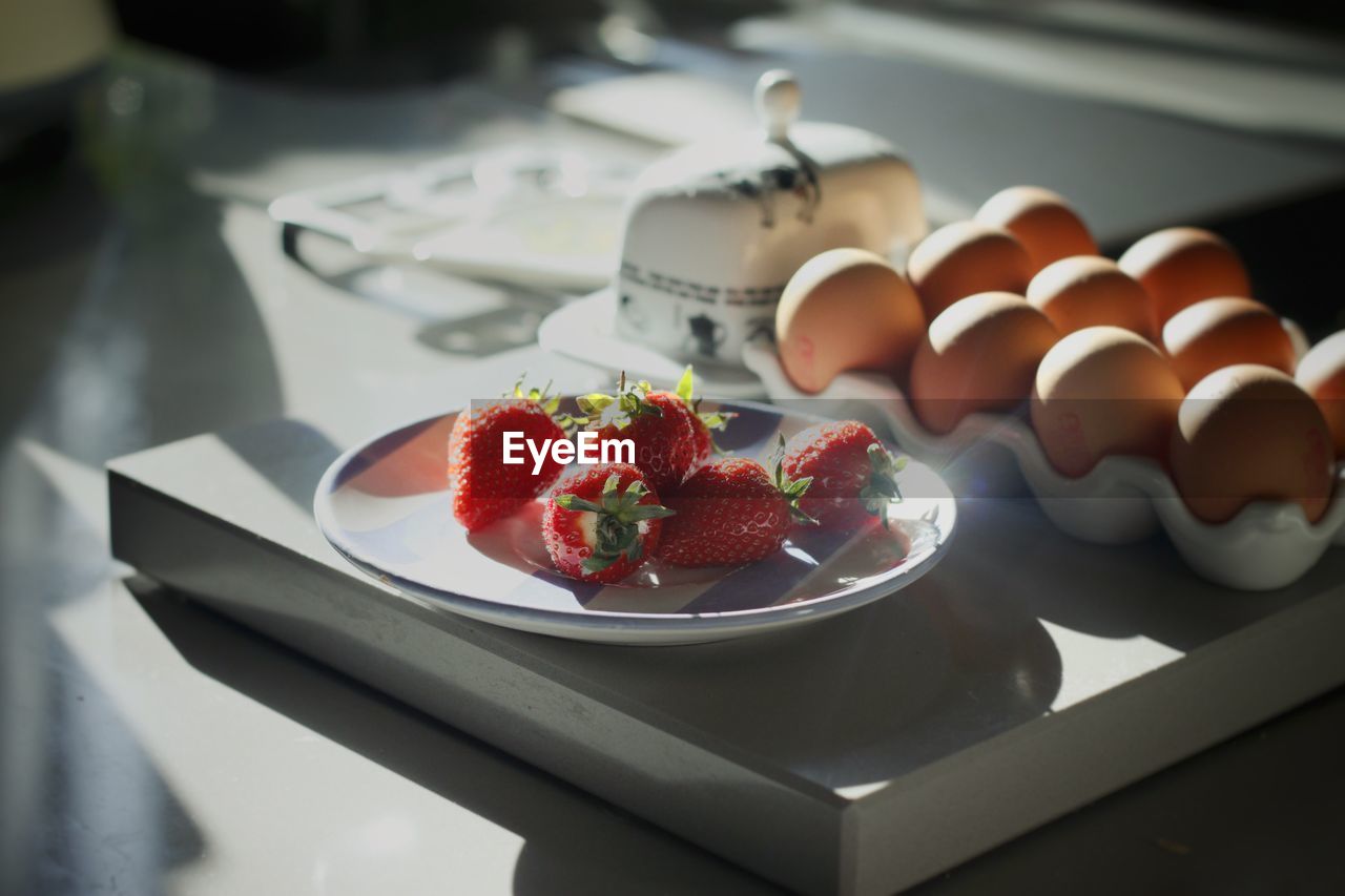 Sunlight falling on eggs in carton by strawberries at table
