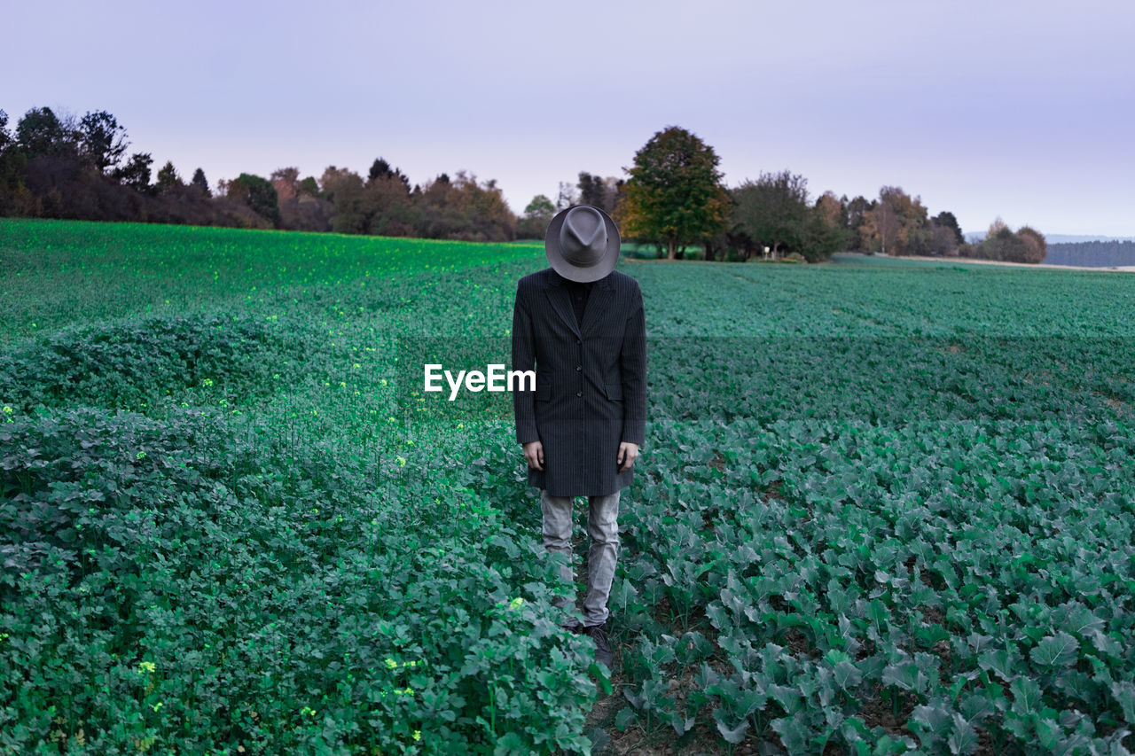 Man with face covered by hat standing on agricultural field