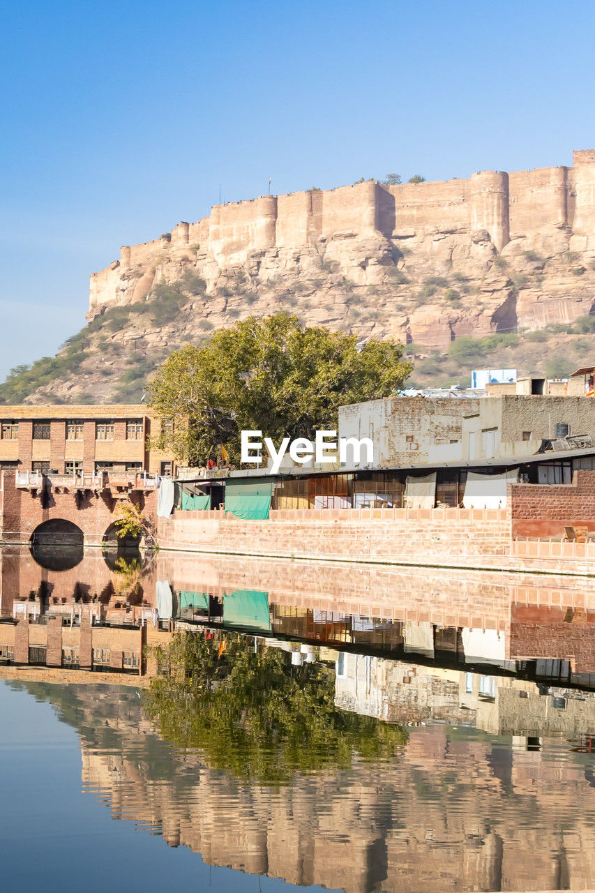 architecture, water, built structure, nature, travel destinations, building exterior, travel, sky, vacation, reflection, clear sky, fortification, building, history, landmark, tourism, no people, town, blue, the past, city, ancient history, river, day, sunny, fort, outdoors, waterfront, tree, land, ancient, plant, wall, mountain, old, house, religion, residential district