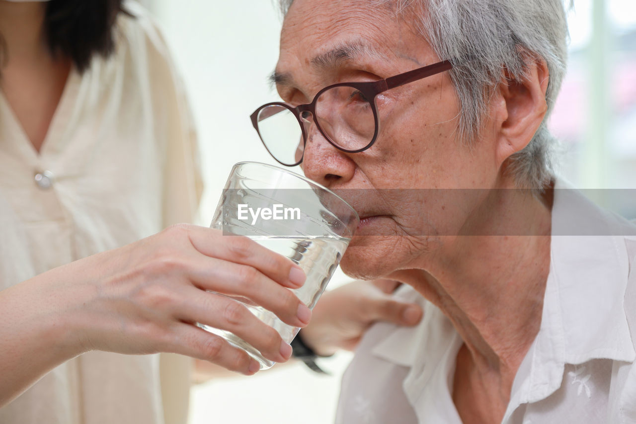 Midsection of nurse feeding water to senior woman