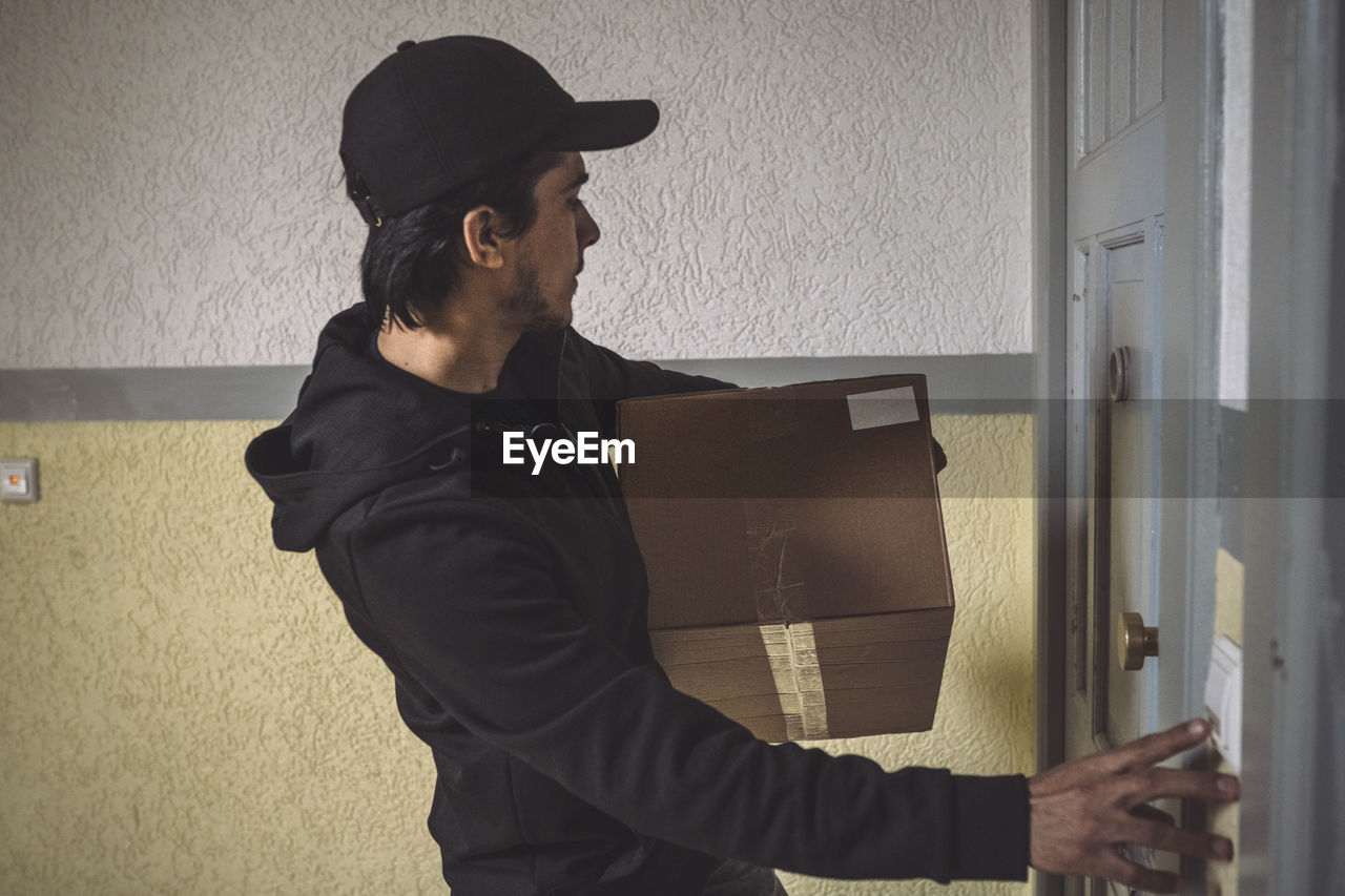 Side view of delivery man with package ringing bell at doorstep