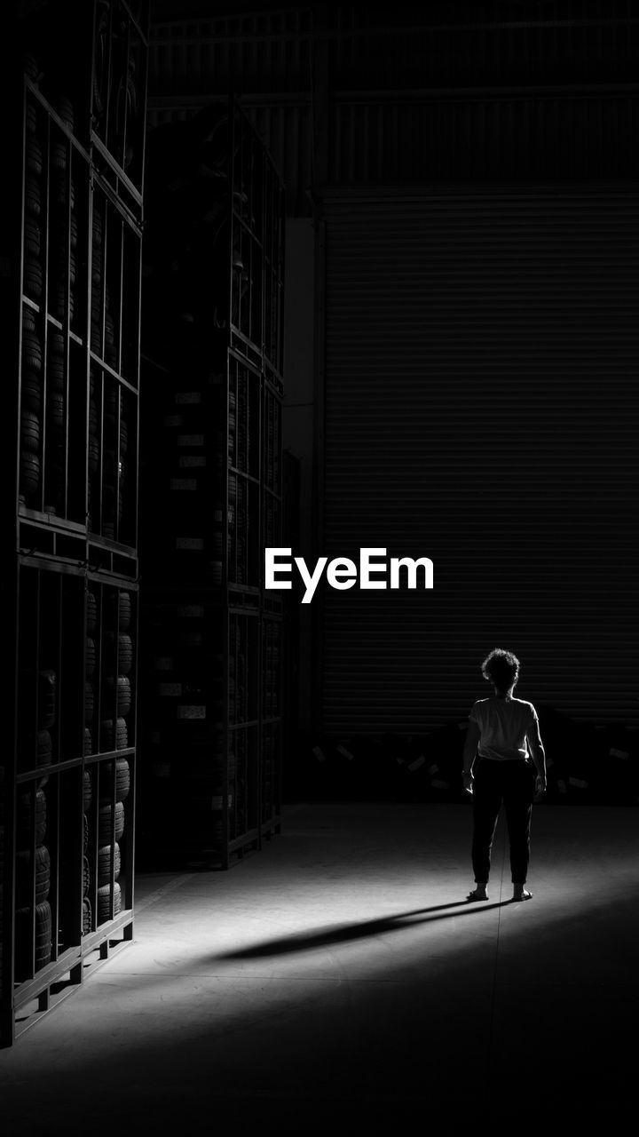 Rear view of woman standing by shelves at night