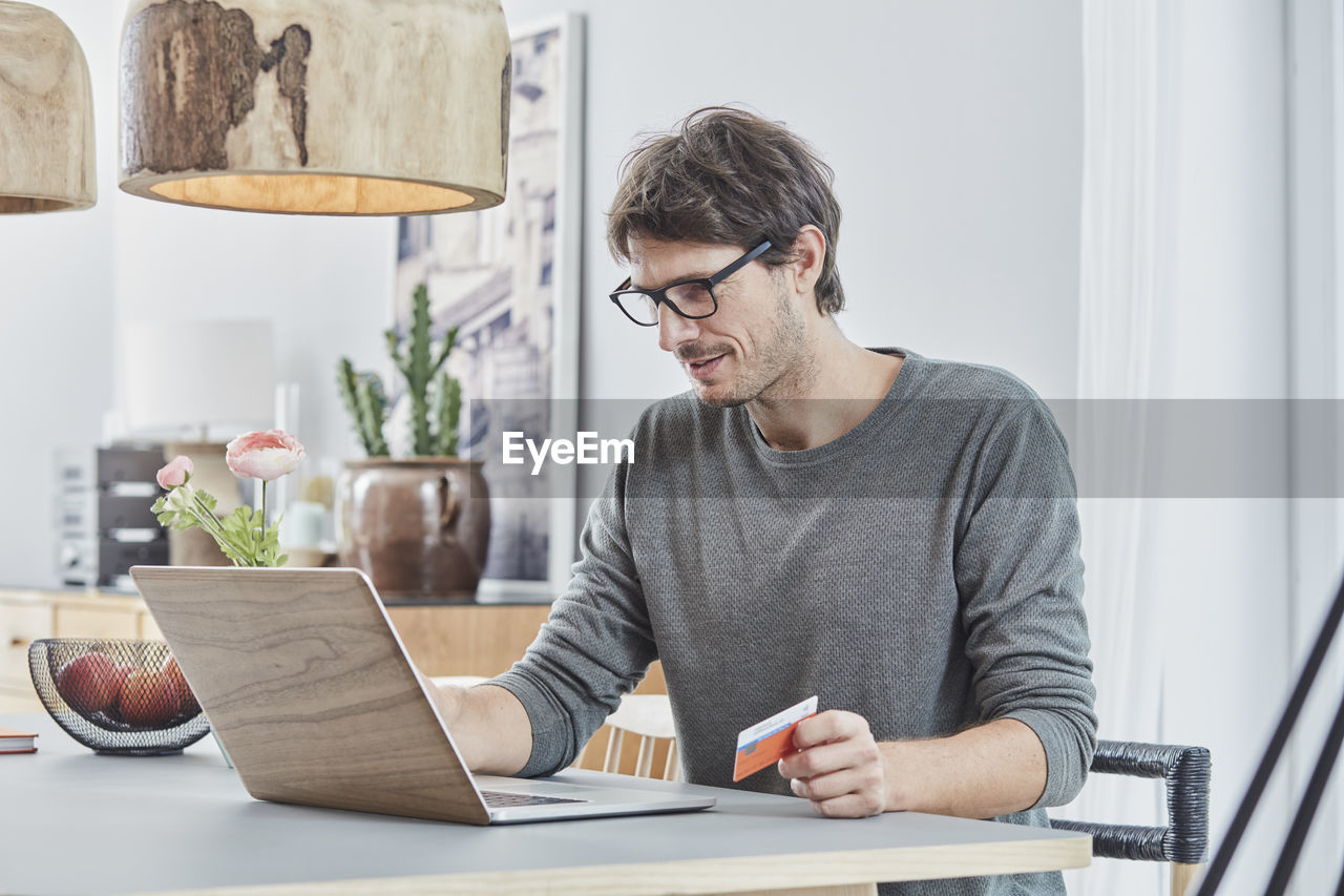 Man holding a card using laptop on table at home