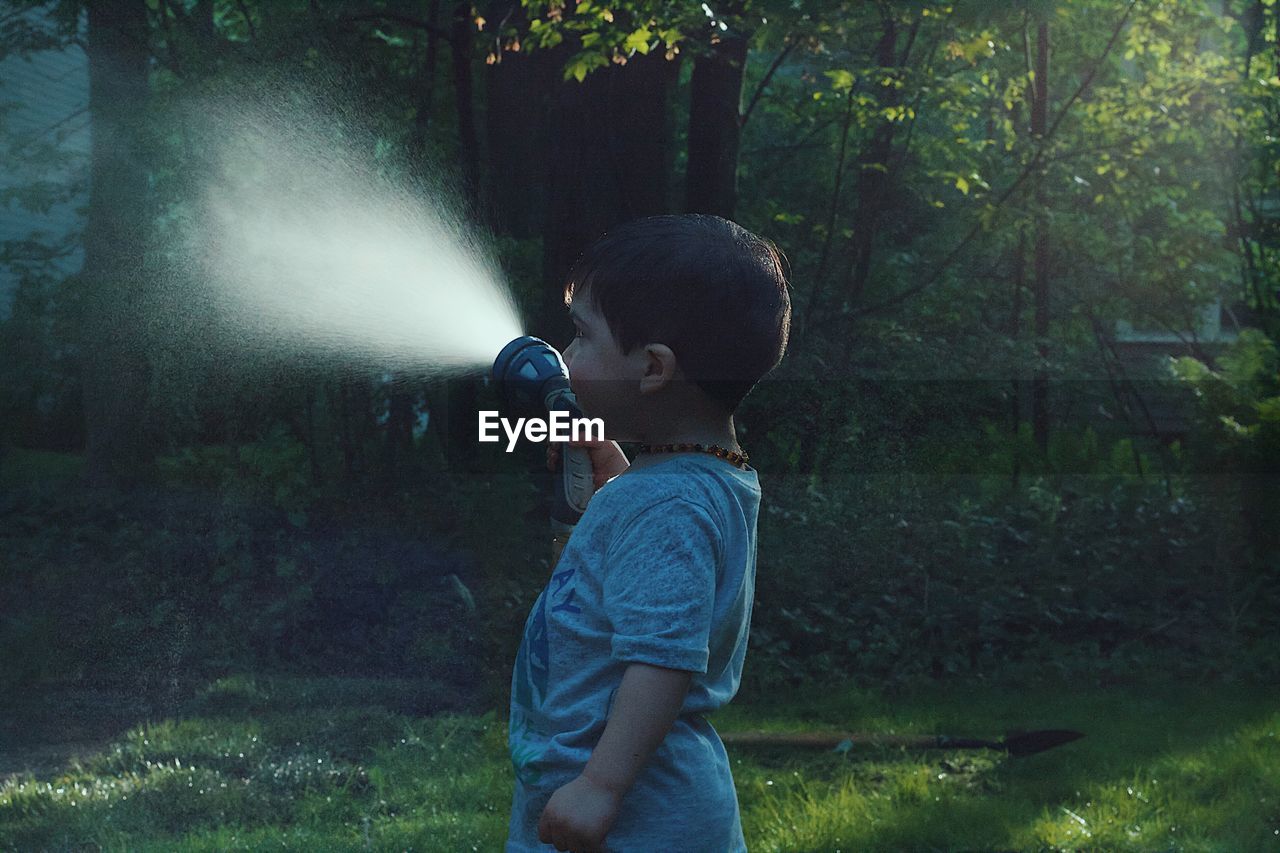 Side view of boy holding garden hose at yard