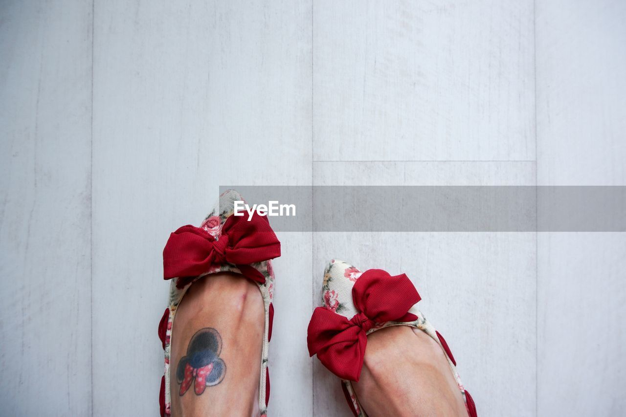 Low section of woman with tattoo wearing red bow shoes