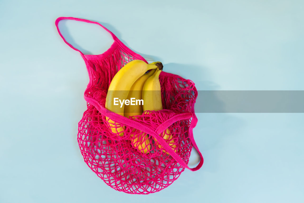 Yellow ripe bananas in a fuchsia eco cotton string bag on a pastel blue background