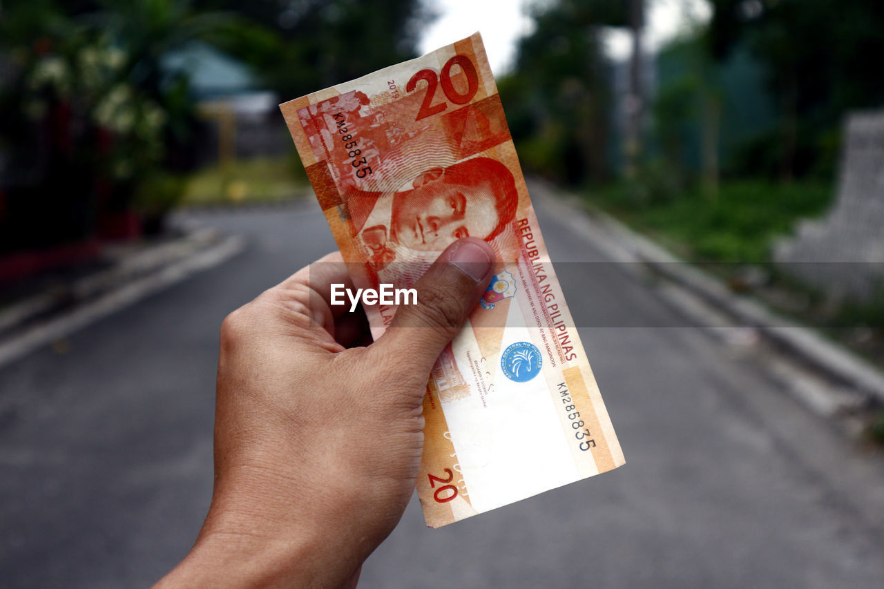 Close-up of hand holding paper currency on road