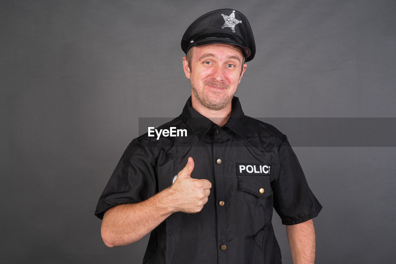 portrait, looking at camera, one person, studio shot, adult, men, protection, clothing, security, authority, occupation, uniform, standing, front view, police force, person, waist up, indoors, law, mature adult, smiling, black, government, beard, emotion, gray background, facial hair, gray, serious, happiness, cap